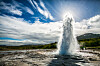 Strokkur-geysiren spruter vann mot en solbelyst, skyet himmel i Island.