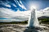 Strokkur-geysiren spruter vann mot en solbelyst, skyet himmel i Island.